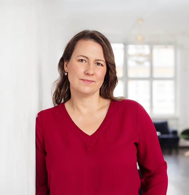 Cordula Stübing lehnt an einer weißen Wand und blickt ruhig in die Kamera.