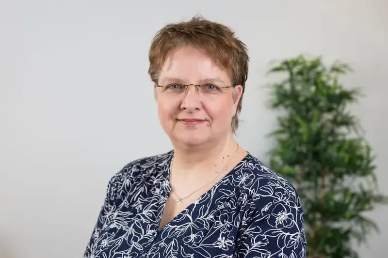 Sandra Hellbusch mit Brille und gemusterter Bluse blickt freundlich in die Kamera.